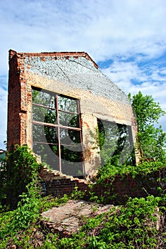 Old crumbling brick wall with window without glass, green trees and blue cloudy sky