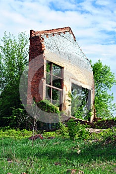 Old crumbling brick wall with window without glass, green trees and blue spring sky