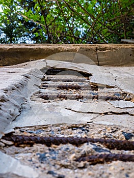Old crumbling concrete wall with exposed and rusty iron reinforcement - Low angle view reveals dense foliage overhanging top of