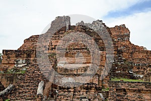 Old crumbling overgrown brick wall in front of stupa at historic park thailand