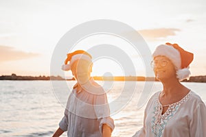 Old cute couple of mature persons enjoying and having fun together at the beach wearing christmas hats on holiday days. Walking on