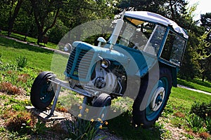 Old Czechoslovak agricultural tractor painted light blue and white, placed as decorative element in park between flower beds