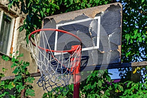 Old and damaged basketball hoop with cage,tree and house in the