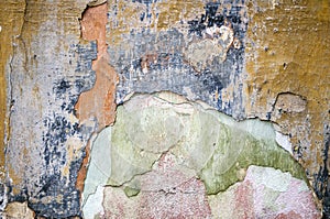Old damaged, cracked wall shows signs of aging along colorful layers