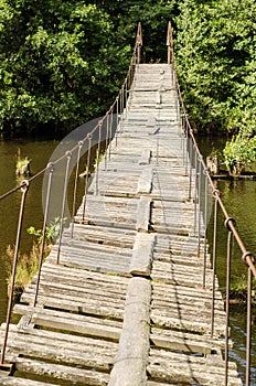 Old and damaged rope and wooden boards bridge over the river Irbe, Latvia
