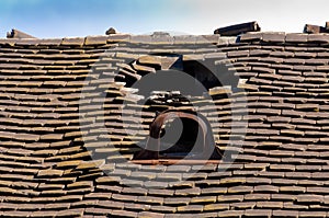 Old damaged tiled roof with a hole on the roof and broken tiles