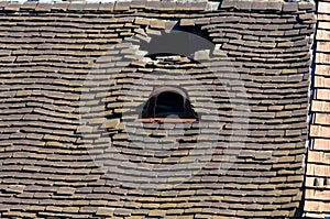 Old damaged tiled roof with a hole on the roof and broken tiles