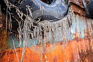 Old, damaged tyre fender with lines sticking out, on a steel hull of an abandoned cargo shipwreck