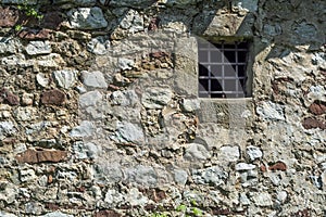 Old dark age stone wall and small prison cell window with bars