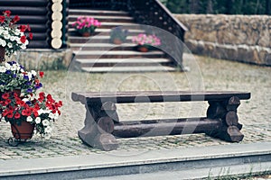 An old dark and low wooden bench on the background of a wooden ladder. There are pots of petunia flowers on the ladders.