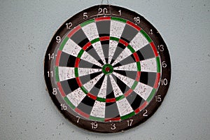 Old dartboard punctured by darts on light wall. Background of an old shabby round target in holes and cuts for game of darts