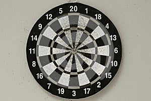 Old dartboard punctured by darts on light wall. Background of an old shabby round target in holes and cuts for game of darts