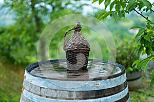 Old demijohn wicker wrapped glass bottle on a barrel