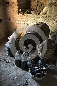 Old demijohns aged wine bottles and wooden barrels in a basement