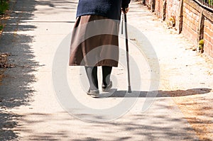 Old depressed woman walk alone down the street with walking stick or cane feeling lonely and lost view from back