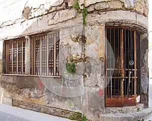 Old derelict abandoned commercial property on a corner with crumbling cracked shabby walls and rusting iron bars across the door