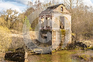 The old destroyed building of the hydroelectric plant with moss-grown walls is located in a forest surrounded by dry grass