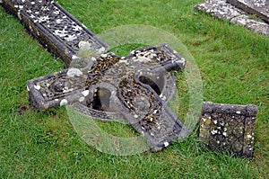 Old destroyed celtic cross in the grass on graveyard