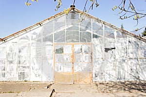 Old destroyed greenhouse with broken window glasses and rusty door. Urban ruined geometry.