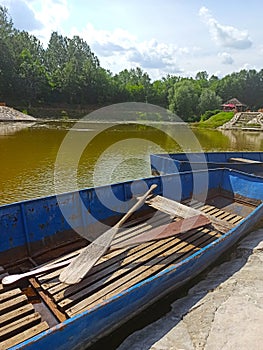 an old, dilapidated, blue boat with wooden oars, by the lake shore