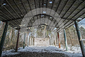 Old dilapidated canopy of abandoned territory in a coniferous forest in winter on a sunny day. The ruins of a former open-air