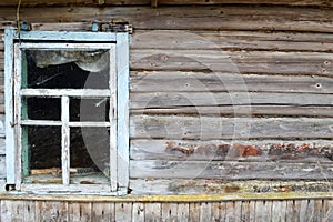 Old dilapidated window of a wooden village house and a wall of dilapidated log