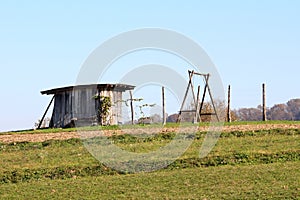 Old dilapidated wooden tool shed with cracked walls next to large wooden frame swing on top of small hill