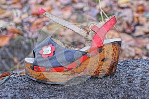 an old dirty colored sandal made of a wooden sole and fabric with a red leather harness