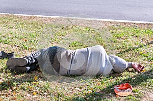 Old dirty drunk or drug addict barefoot homeless or refugee man sleeping on the grass in the street social documentary concept