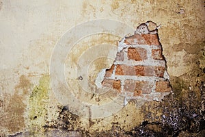 Old dirty and grungy plastered wall facade of an abandoned house with a hole showing the underlying red bricks