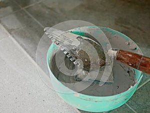 Old dirty grungy trowel in a plastic bowl with tile grunt - tools for grunting the ceramic tile floor - tiling work