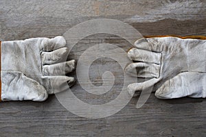 Old dirty leather work gloves on wood background, engineering equipment concept