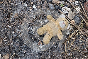 Old dirty teddy bear neglected on the ground soil. End of childhood