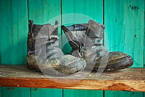 Old dirty torn shoes stand on a wooden shelf against the background of a green wall