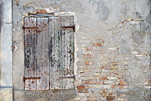 Old dirty wall with closed window with shutters. Aged italian street wall background with bricks and plaster