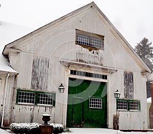 Old dirty white New England barn with green doors and multi-panel doors