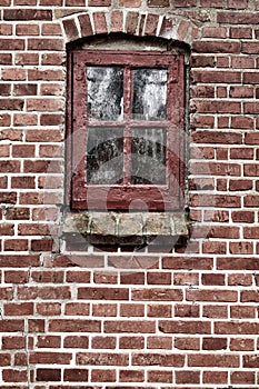 Old dirty window in a red brick house or home. Ancient casement with red wood frame on a historic building with clumpy