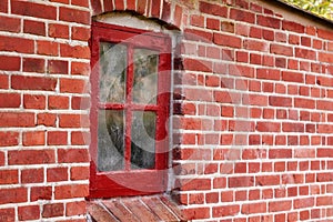 Old dirty window in a red brick house or home. Ancient casement with red wood frame on a historic building with clumpy photo