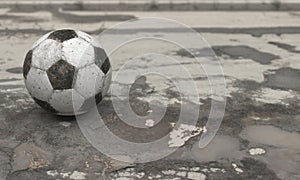 An old dirty worn ball lies on wet cracked asphalt with pits and puddles on a cloudy rainy day. 3D rendering illustration with