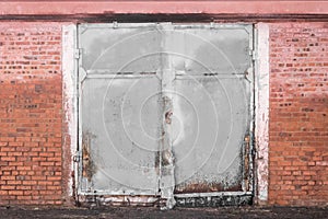 Old dirty worn weathered iron warehouse door with brick wall of building abandoned architecture