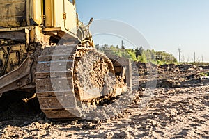 Old dirty yellow crawler bulldozer, rear view, the construction machine is lit by the rays of the setting sun