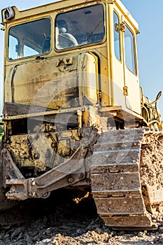 Old dirty yellow crawler bulldozer, rear view, the construction machine is lit by the rays of the setting sun