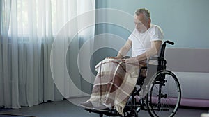 Old disabled man sitting in wheelchair and looking in window, waiting for son