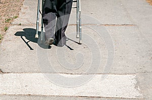 Old disabled woman walking alone and depressed on the street in the city helped by adjustable walker stick or cane