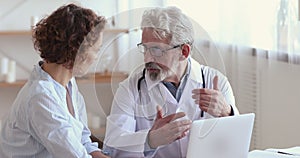 Old doctor consulting female patient showing test results on laptop