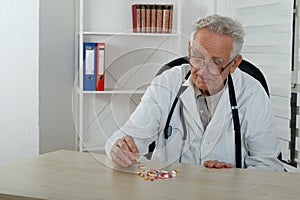 Old doctor observe colorfully pills in consulting room