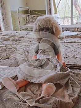 An old doll with a dirty face on a bed in an abandoned kindergarten. Radiation-contaminated room in Chernobyl