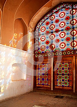 Old door with colored glass and reflection of colored lights inside Dolatabad Garden, Yazd, Iran