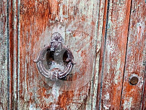 Old door knocker on an old wooden door with peeling paint