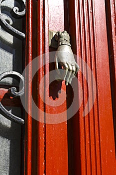 Old doorknocker with hand shape on red wooden door